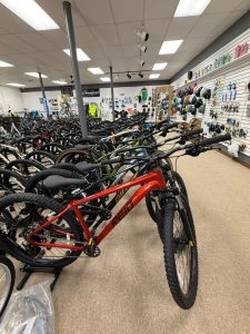Rows of bicycles in shop showroom with red mountain bike in foreground and wall of helmets and accessories