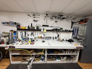 Bicycle repair workbench with pegboard wall holding organized tools, lubricants, and parts in a workshop